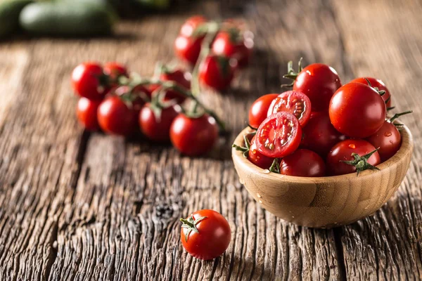 Tomates cherry frescos en un tazón de madera sobre una mesa de roble viejo —  Fotos de Stock