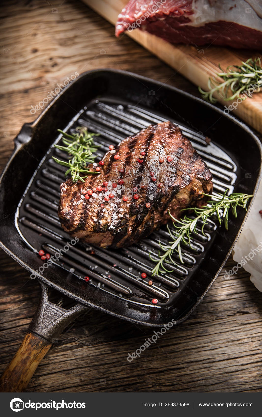 Grilled beef steak in grill pan with herbs rosemary on wooden table