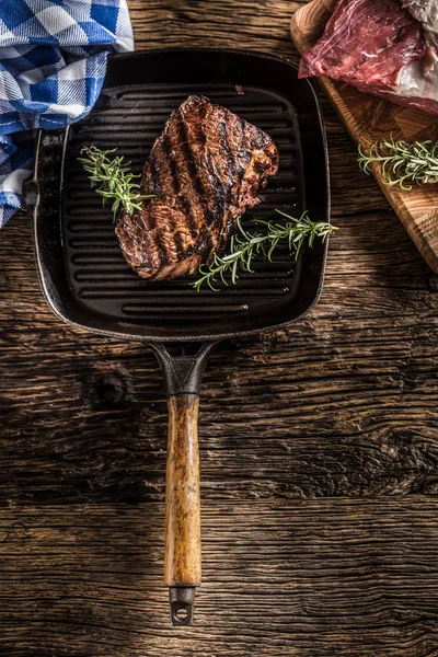 Stek wołowy z grilla w patelni z rozmarynem zioła na drewnianym stole — Zdjęcie stockowe