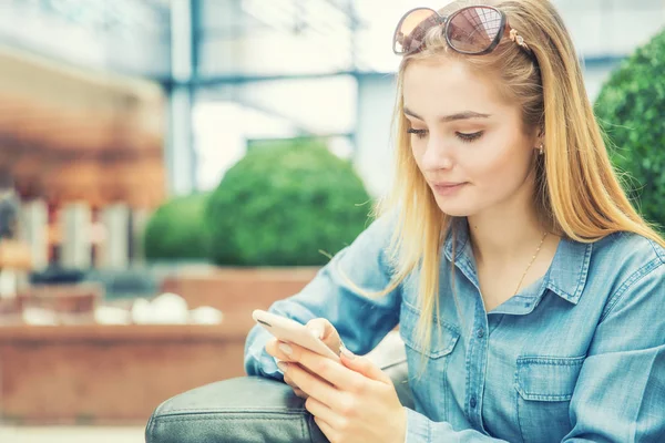 Chica mensajes de texto en el teléfono inteligente en un centro comercial de afeitar sentado en int — Foto de Stock