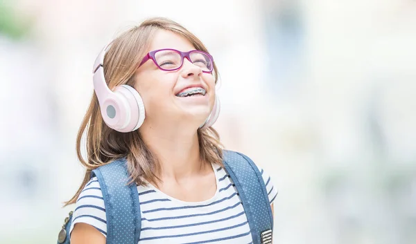 Gelukkig lachende schoolmeisje met tandheelkundige accolades en glazen listenin — Stockfoto