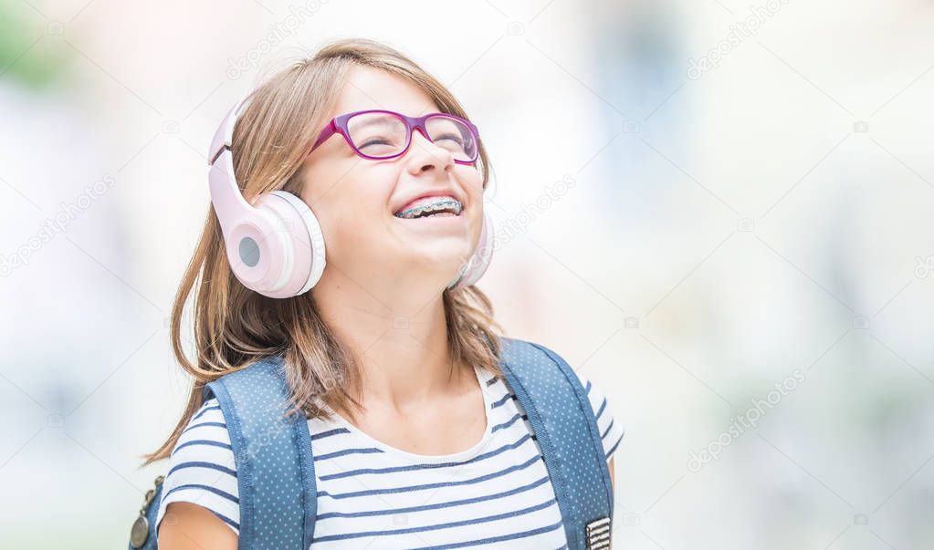 Happy smiling schoolgirl with dental braces and glasses listenin