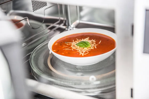 Inside view of new clean staniless microwave oven with a tomato soup in white plate — Stock Photo, Image