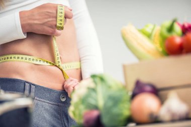 Bel ölçü bandıyla tahta kutunun üzerinde sebzeli bir kadın.