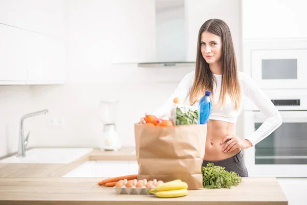 Jovem mulher de pé na cozinha com compra na mesa — Fotografia de Stock