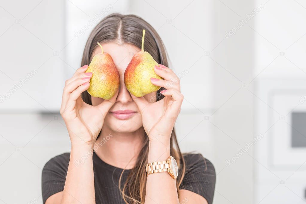 Young woman in home kitchen looking over two pears