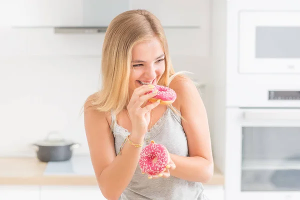 Jeune fille blonde mange des beignets roses dans la cuisine à la maison avec goût em — Photo