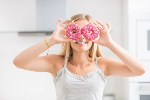 Giovane ragazza coperto il viso con ciambelle rosa in cucina a casa. Em. — Foto Stock