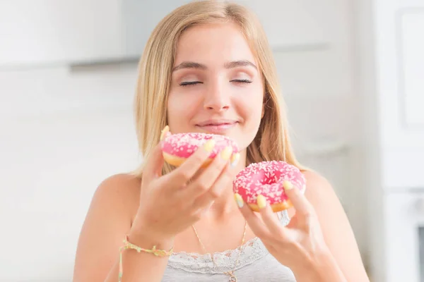 Young blonde girl eats pink donuts in home kitchen with taste em — Stock Photo, Image