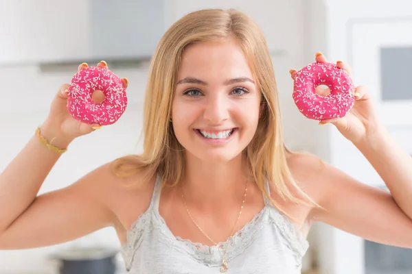 Joven chica rubia come rosados donuts en casa cocina con gusto em —  Fotos de Stock