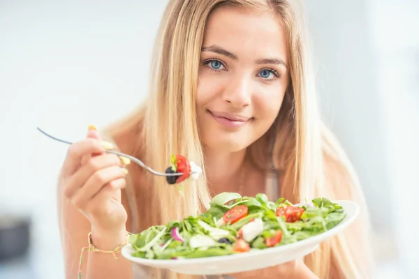 Joven chica rubia feliz comiendo ensalada saludable de rúcula espinaca —  Fotos de Stock