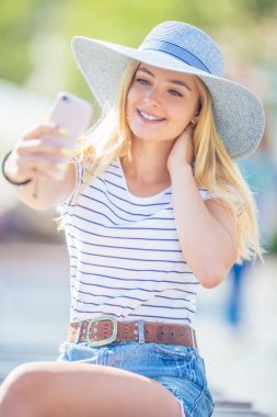 Parkta akıllı telefonla oturmuş selfie çeken genç kadın. Summ