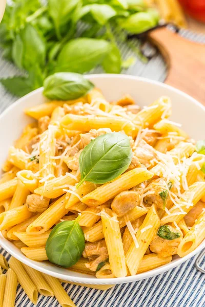 Pasta penne com pedaços de frango cogumelos manjericão queijo parmesão e vinho branco. Comida italiana em prato branco na mesa da cozinha — Fotografia de Stock