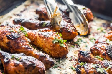 Pişmiş kağıt üzerinde baharat otlar ve susam ile ızgara hicken bacaklar BBQ. Kavurucu çanak kavrulmuş kümes hayvanları yemek