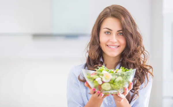 Giovane donna che tiene ciotola con insalata nella sua cucina. Vita sana — Foto Stock