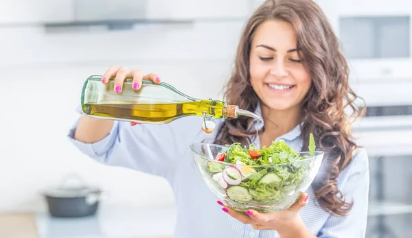 Giovane donna che versa olio d'oliva nell'insalata. Stile di vita sano — Foto Stock