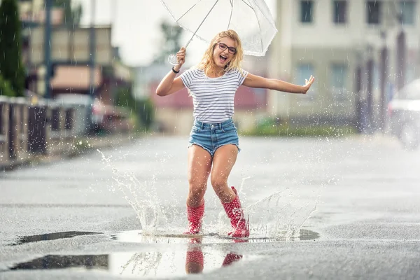 Veselá dívka skákající s bílým deštníkem v tečkované červené galoši — Stock fotografie