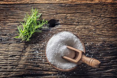 Eski bir meşe masada bir kepçe ile ahşap bir kapta biberiye otlar ile kaba taneli tuz