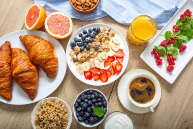 Yoğurt müsli yaban mersini çilek ve muz tabağı ile servis edilen sağlıklı kahvaltı.