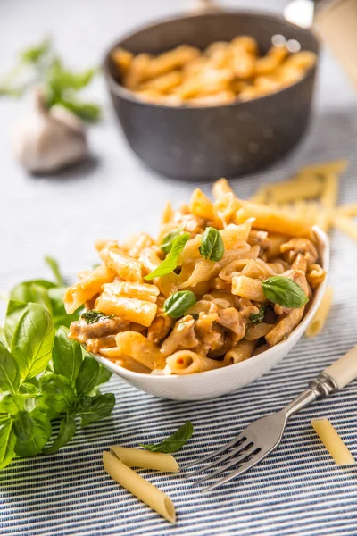 Penne de pasta con trozos de pollo setas albahaca y queso parmesano comida italiana en tazón blanco en la mesa de la cocina —  Fotos de Stock