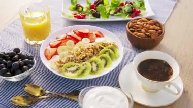 Müsli granola 'dan sağlıklı kahvaltı taze meyveli kivili çilek suyu yoğurt suyu ve kahve. Ham formatta Siyah Sihirli Sinema 6k kamerasında yavaş çekim.