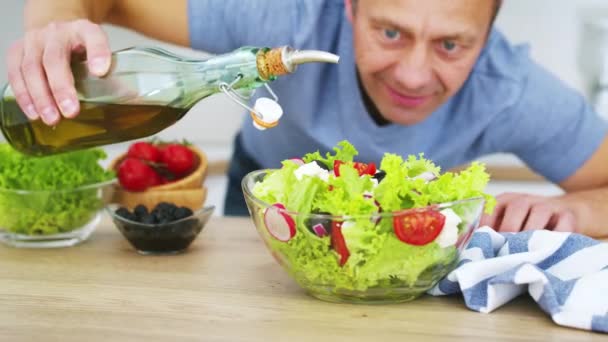 男は台所の新鮮な野菜サラダにオリーブオイルを注ぐ料理 スローモーションビデオ Black Magic Cinemaカメラ6K Raw形式 — ストック動画