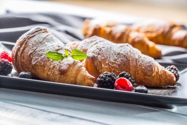 Taze çıtır kruvasanlar üzerine ahududu böğürtlen ve yaban mersini serpiştirilmiş şeker tozu serpiştirilmiş.
