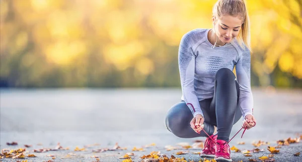 Mujer corredora atando cordones de zapatos antes de correr en el callejón del árbol de otoño — Foto de Stock