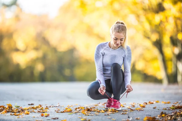 Ženská běžkyně svazuje tkaničky před joggováním v podzimní uličce — Stock fotografie