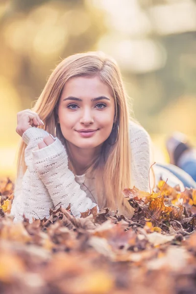 Autumn portrait of young woman lying on maple leaves in park — Stock Photo, Image