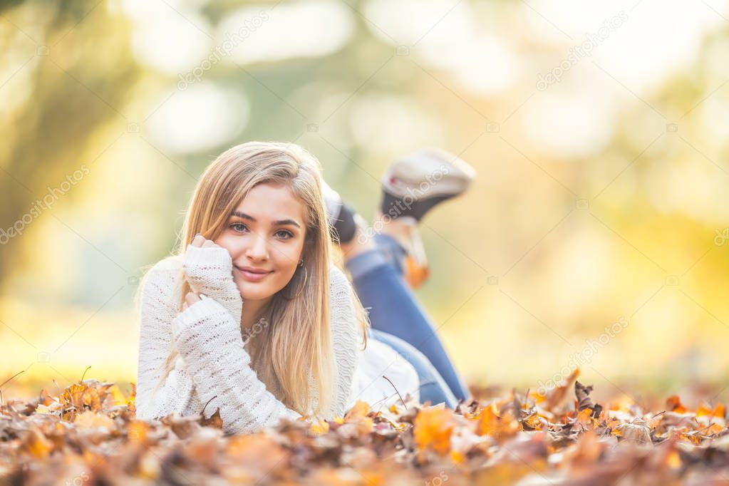 Autumn portrait of young woman lying on maple leaves in park