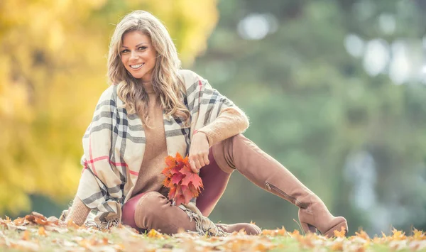 Привлекательная молодая женщина с чувственной улыбкой сидит в осеннем парке — стоковое фото