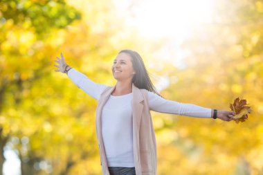 Sonbahar parkındaki mutlu kadın elinde yapraklarla buket tutuyor.