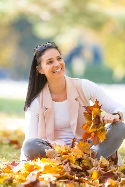 Mujer feliz sentada en el parque de otoño sosteniendo ramo con otoño —  Fotos de Stock