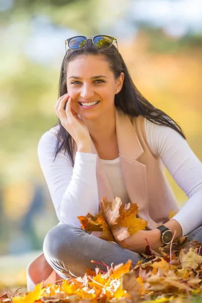 Mujer feliz sentada en el parque de otoño sosteniendo ramo con otoño —  Fotos de Stock