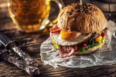 Kıymalı hamburger, sahanda yumurta ve pastırma, salata, yanında kırsal bıçakla biber ve fıçı bira.