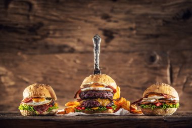 Çifte sığır etli burger, tavuk burger ve en büyük hamburgerin içine saplanmış eski bir bıçakla kırsal ahşap bir ortamda sığır burger.