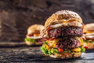 Arka planda iki hamburger daha olan, klasik bir ortamda erimiş peynirli, leziz bir çift etli burger.