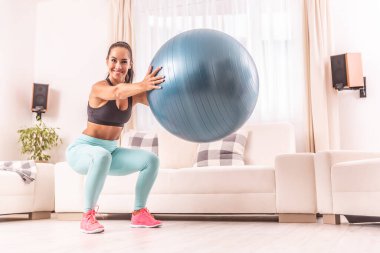 Evde güzel, zayıf bir sporcunun önünde duran bir topla çömelmek..