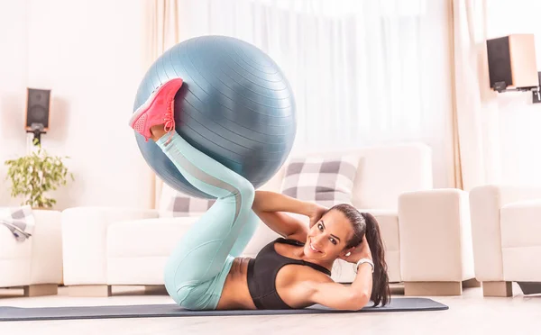 一个漂亮的女运动员在家里用一个合适的球来做腹肌运动 — 图库照片