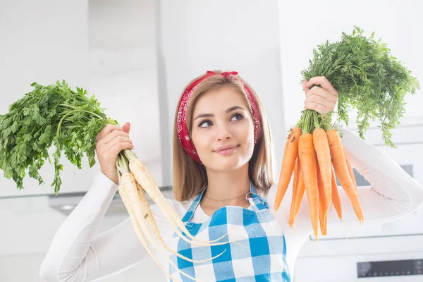漂亮的姑娘在厨房里拿着一捆捆新鲜的胡萝卜和欧芹 — 图库照片