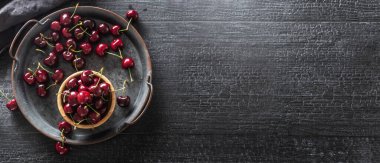 Metalik vintage tepsi, yüzey ve fincanın içinde kırmızı sulu kirazlar var ve tepsinin etrafına saçılmış.