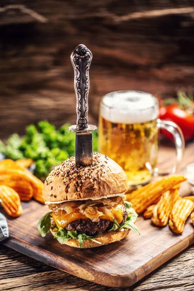Beef burger with caramelized onion and arugula in a rustic wooden environment, a beer and potato wedges on the side
