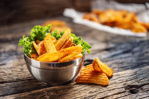 Koyu ahşap üzerinde salata yaprağı olan metal bir kasede kıtır kıtır patates parçaları. — Stok fotoğraf