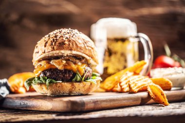Karamelli soğanlı biftek, roka ve patates dilimli erimiş peynir ve arka planda bira.