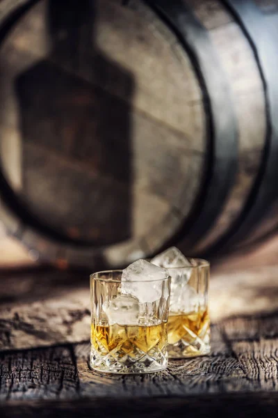 Twee kopjes whisky op rustiek hout en een schaduw van een fles weerspiegeld op een houten vat — Stockfoto