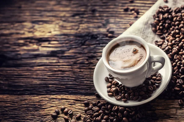 작은 나무 탁자 위에 커피콩이 흩어져 있는 자기 컵에 들어 있는 검은 커피 — 스톡 사진