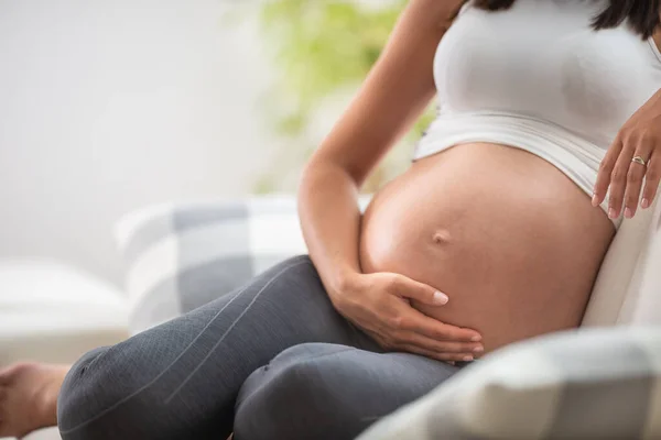 妊娠中の女性の腹部の詳細は ソファの上に座って それを上に手で — ストック写真