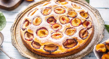 Ev yapımı erikli kek, ahşap masada eski bir tabakta. Şeker tozlu erik turtası