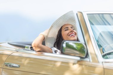 Sağ elini kullanan, gözleri kapalı, başını arkaya eğmiş, şapkasını tutuyor ve yaz gezintisinin tadını çıkarıyor..